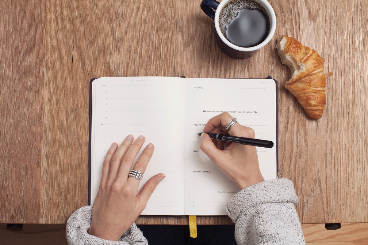 Escrevendo diário em uma mesa com um café e um croissant